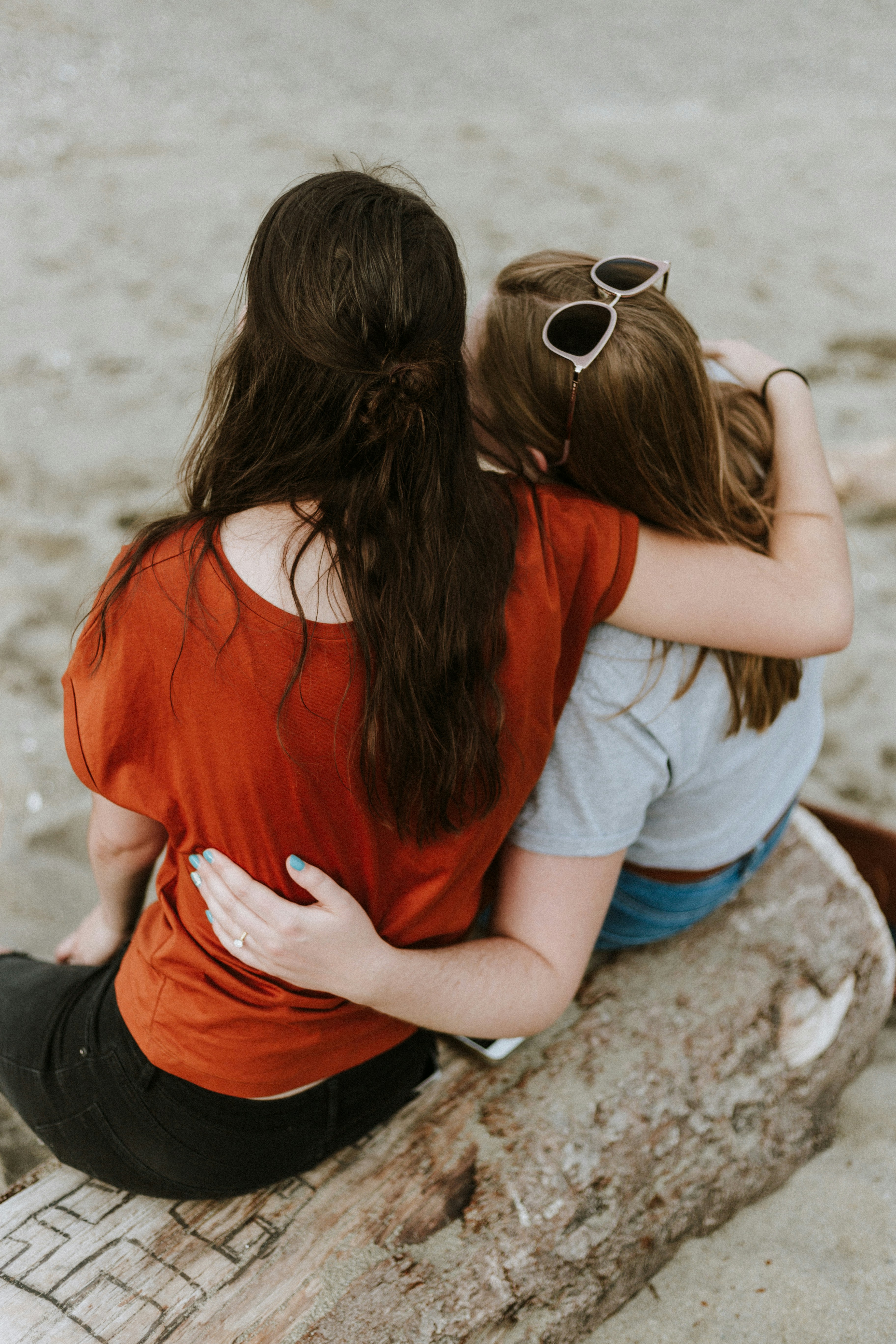Two people sitting close together with an arm around each other in a quiet outdoor setting.