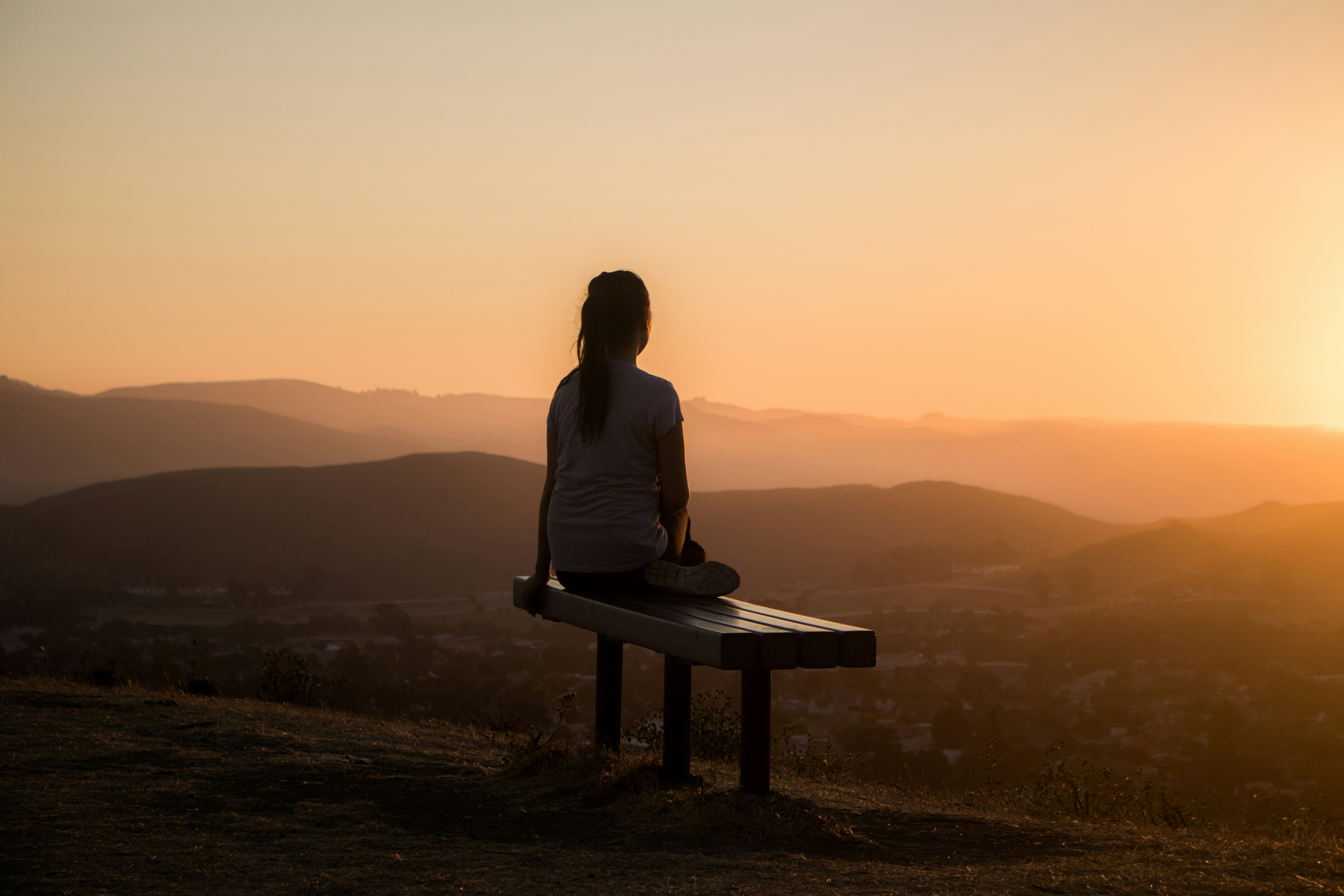 A person sitting on a bench at sunset overlooking rolling hills.